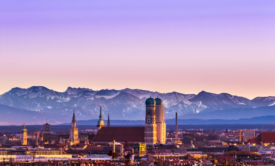 Blick auf München mit Frauenkirche und schneebedeckten Alpen im Morgenlicht